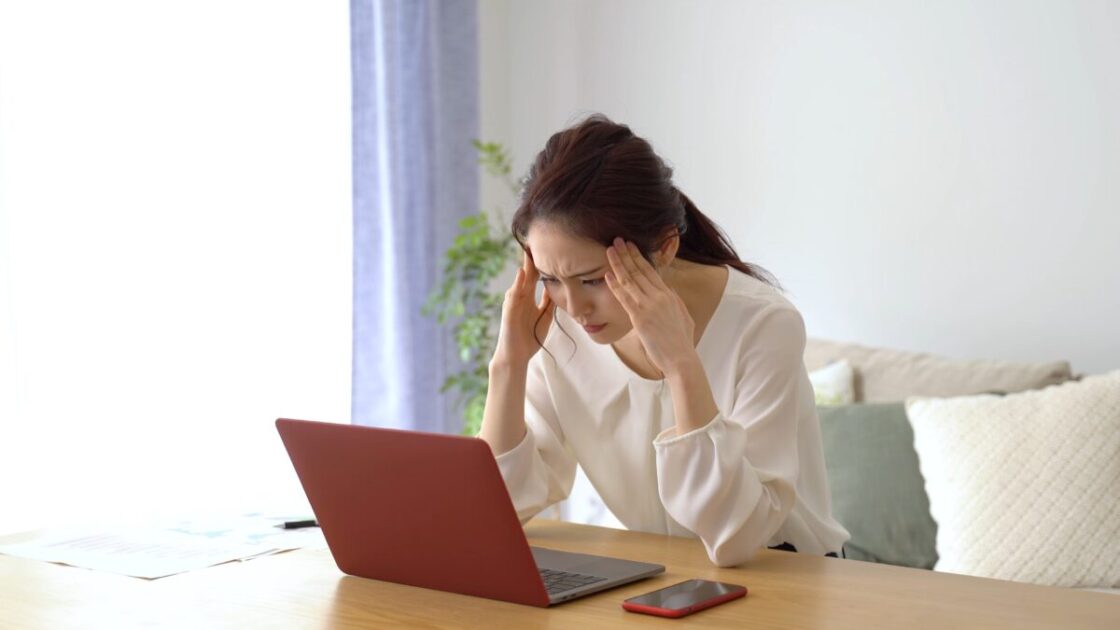 パソコンの前で頭を抱えている人の画像